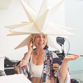 Daniela DJing in a white paper star headpiece, laughing