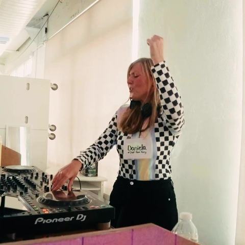 DJ Daniela with a hand in the air behind the DJ booth